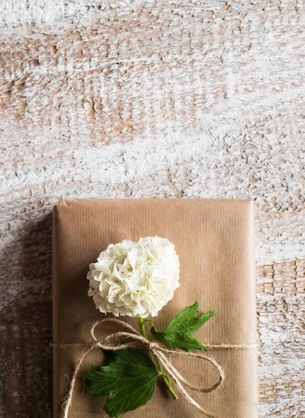 Δώρο τυλιγμένο σε καφέ χαρτί, λιλά λουλούδι χορήγησης. — Φωτογραφία Αρχείου