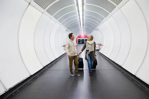 Casal sênior no corredor do metrô puxando bagagem de carrinho . — Fotografia de Stock