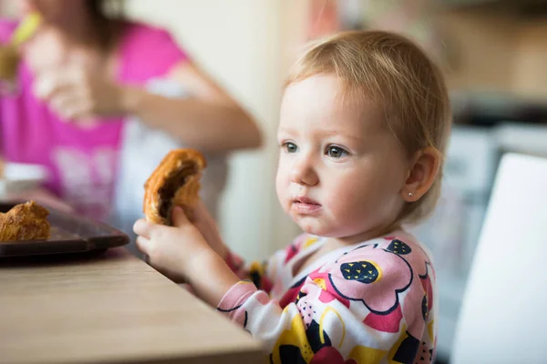 Linda niña sentada en la mesa comiendo croissant —  Fotos de Stock