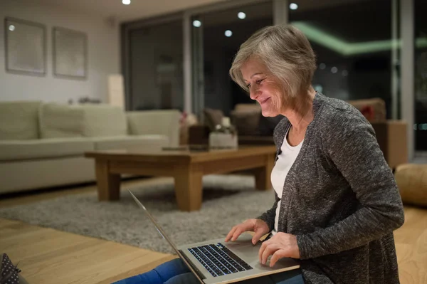Пожилая женщина, сидящая на полу и работающая на ноутбуке — стоковое фото