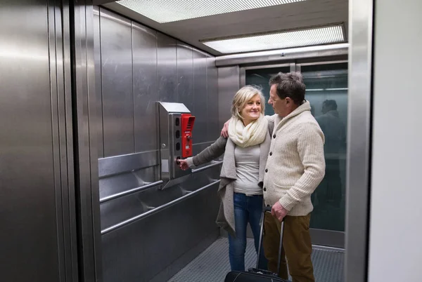 Beautiful senior couple with luggage standing in modern elevator — Stock Photo, Image