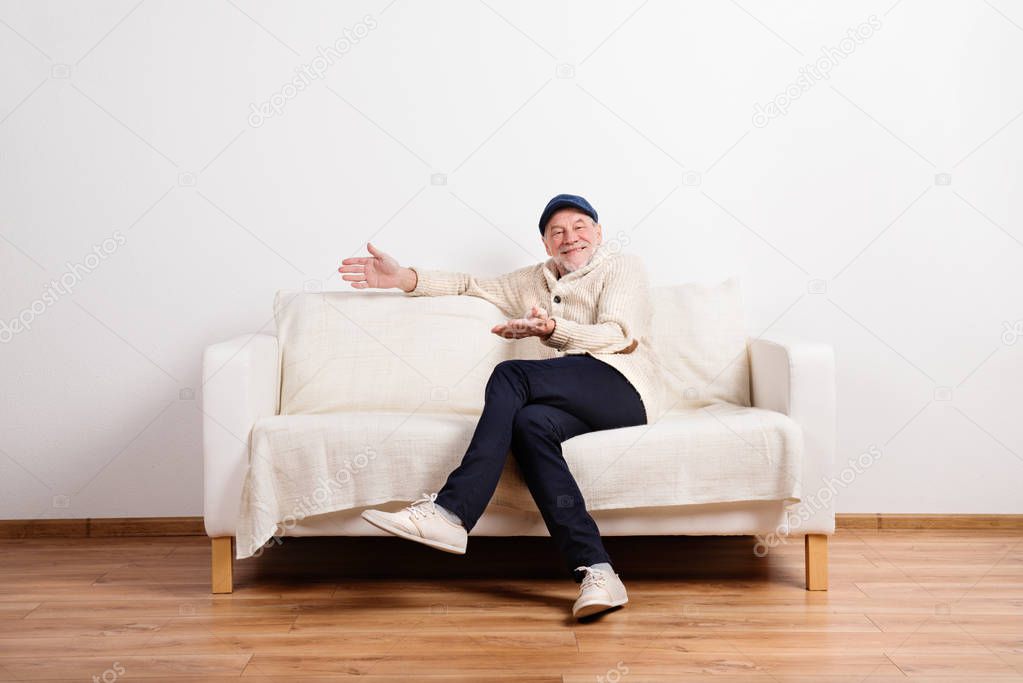 Senior man in beige sweater sitting on sofa, studio shot.
