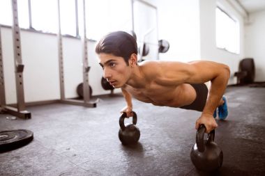 Genç yerleştirmek İspanyol adam gönderme yapıyor spor salonunda ups kettlebells üzerinde