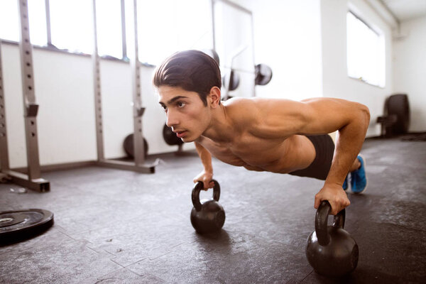 Young fit hispanic man in gym doing push ups on kettlebells