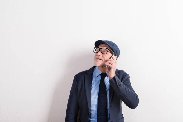 老人在蓝色衬衫、 外套、 眼镜和帽子，拿着智能手机. — 图库照片