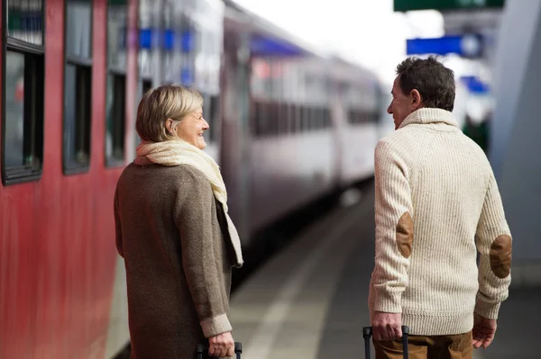 Coppia anziana sulla stazione ferroviaria tirando carrello bagagli . — Foto Stock