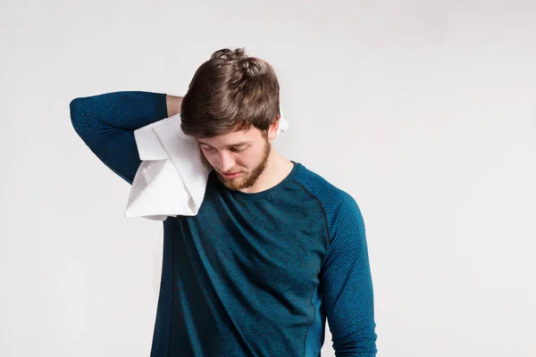 Schöner Fitnessmann, der sich nach dem Training ausruht, Handtuch um den Hals legt und sich den Schweiß abwischt. Studioaufnahme auf grauem Hintergrund. — Stockbild Schöner Fitness-Mann, der sich nach dem Training ausruht, Handtuch um nec — Stockfoto