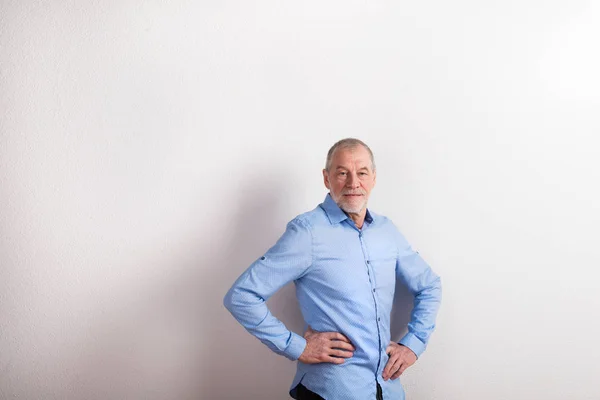 Senior man in licht blauw shirt, glimlachen, wapens op heupen, studio sho — Stockfoto