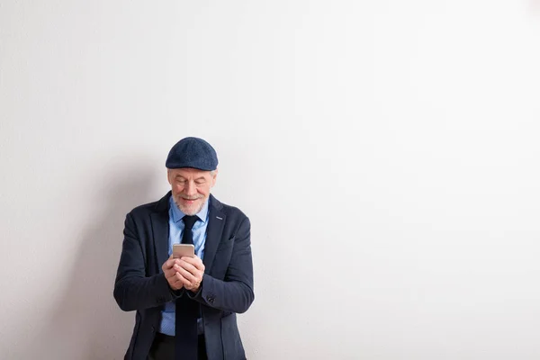 Старший мужчина в пиджаке, очках и кепке, держит смартфон — стоковое фото