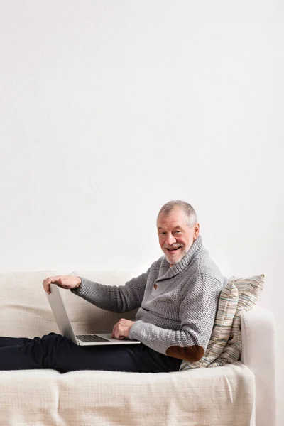 ラップトップに取り組んで、ソファーに座っていた年配の男性. — ストック写真