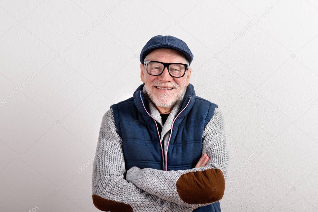 Senior man in sweater, vest jacket and cap, studio shot.