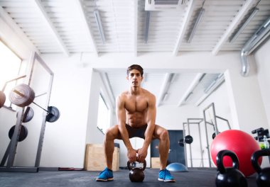 Genç İspanyol adam kettlebell salıncaklar yapıyor spor salonunda yerleştirmek.