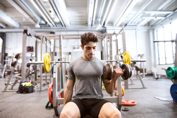 Hombre hispano en el gimnasio sentado en el banco, haciendo ejercicio con pesas — Foto de Stock
