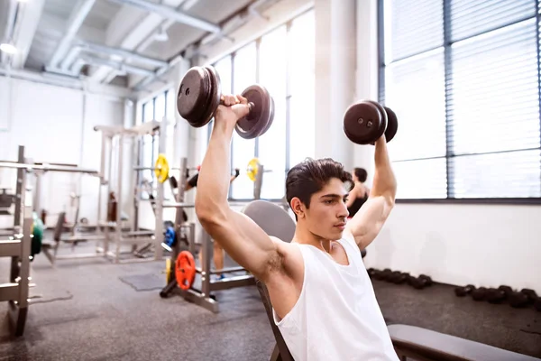 Hombre hispano en el gimnasio sentado en el banco, haciendo ejercicio con pesas —  Fotos de Stock