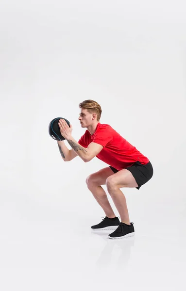 Fitnessmann hält Medizinball, macht Kniebeuge, Studioaufnahme. — Stockfoto