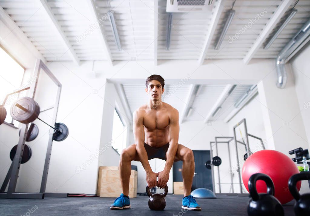 Young fit hispanic man in gym doing kettlebell swings