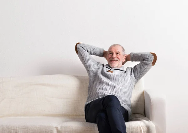 Senior man in grijze trui zittend op de Bank, studio opname. — Stockfoto