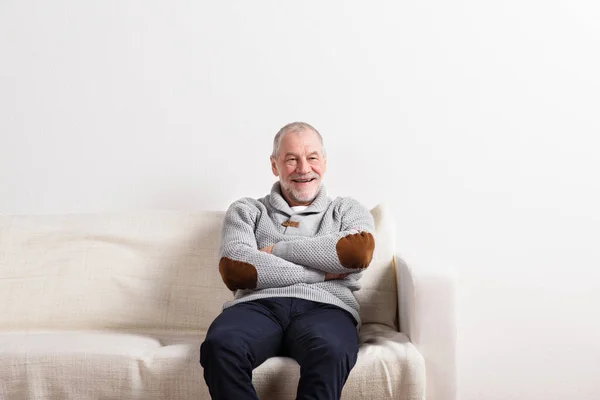 Uomo anziano in maglione grigio seduto sul divano, ripresa in studio . — Foto Stock
