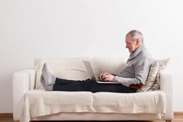 Старший чоловік сидить на дивані, працює на ноутбуці . — стокове фото