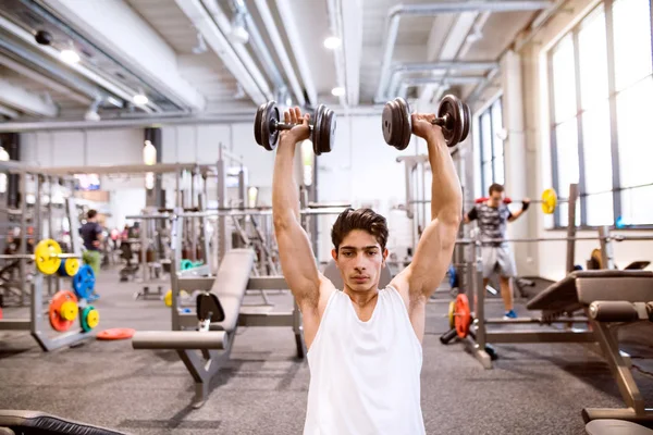Spanischer Mann im Fitnessstudio sitzt auf Bank und trainiert mit Gewichten — Stockfoto