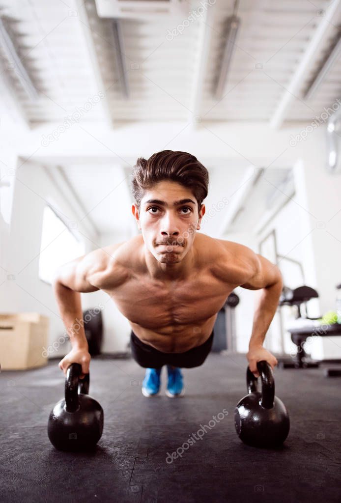 Young fit hispanic man in gym doing push ups on kettlebells