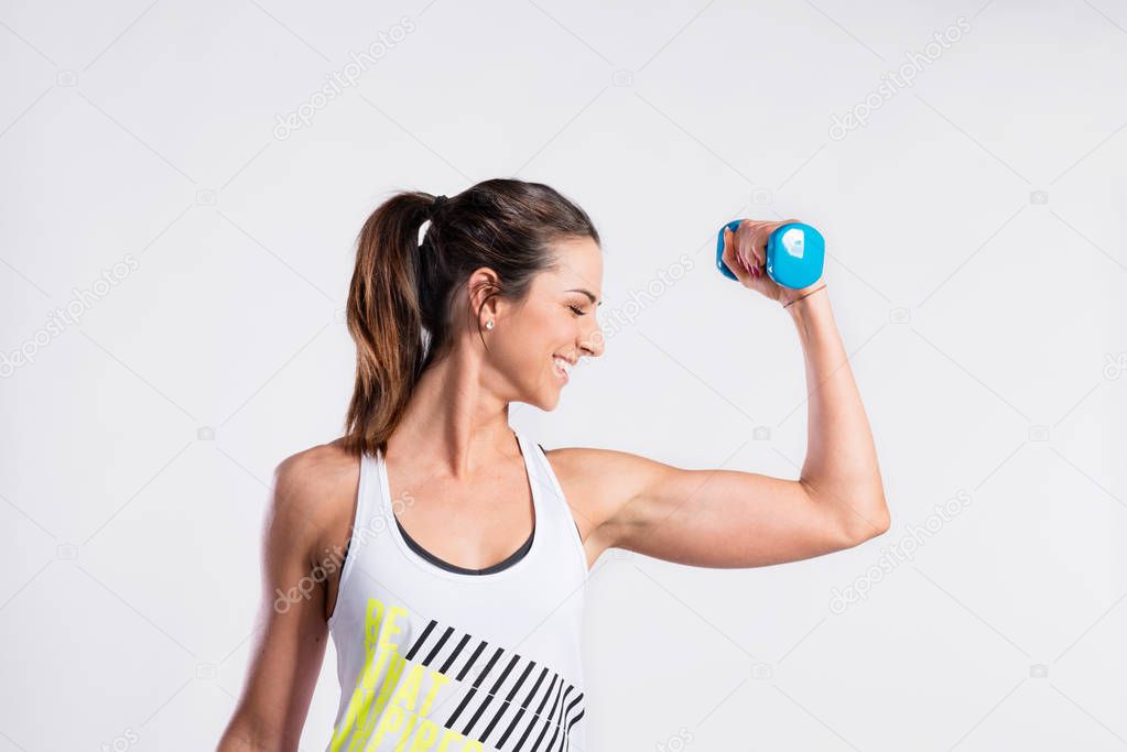 Attractive young fitness woman holding dumbell. Studio shot.
