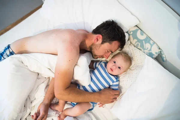 Junge liegt im Bett, sein Vater umarmt ihn — Stockfoto