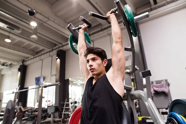 Spansktalande man utbildning i gym, gör maskinen axeln trycker du. — Stockfoto