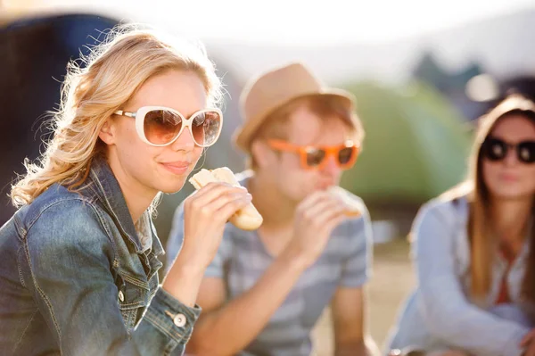 Teenagers sitting on the ground in front of tents and eating — Stock Photo, Image