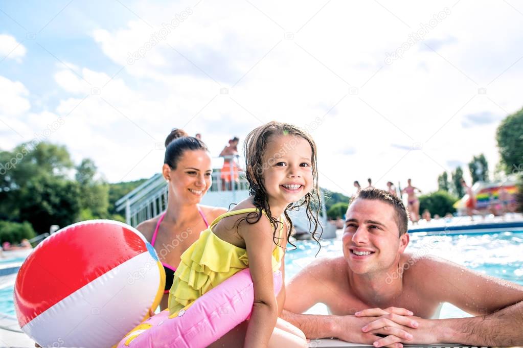 Mother, father and daughter in swimming pool. Sunny summer.