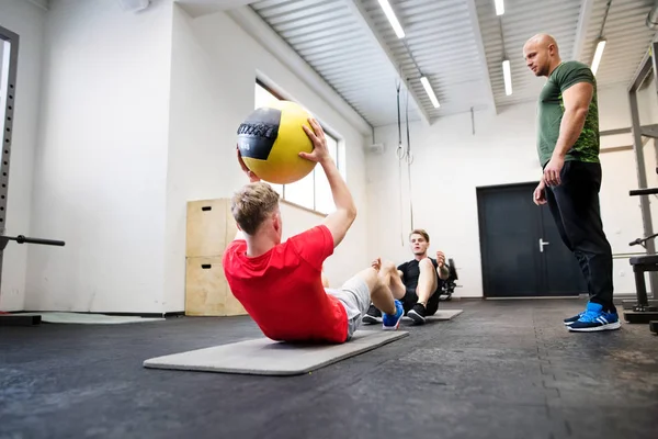 Hommes en gymnase avec entraîneur faisant de l'exercice avec des boules de médecine . — Photo