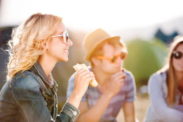 Teenagers sitting on the ground in front of tents and eating — Stock Photo, Image