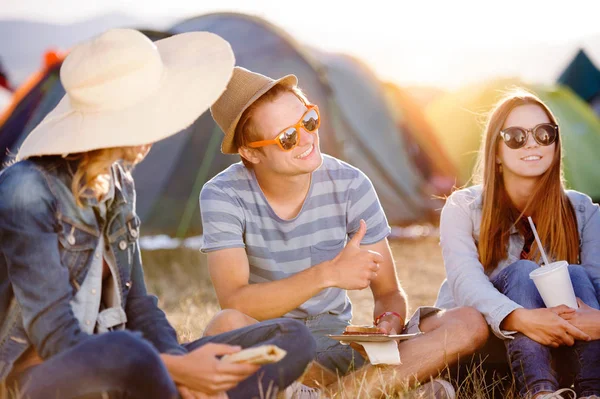 Teenagers sitting on the ground in front of tents and eating — Stock Photo, Image