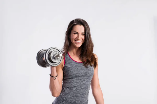 Fitness kvinna anläggning dumbell. Studio skott, grå bakgrund. — Stockfoto