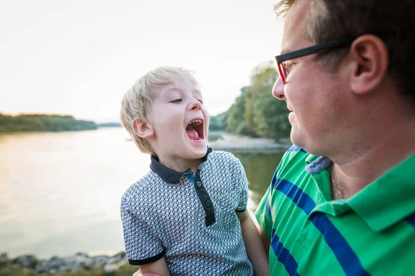 Unga far med liten pojke vid sjön, solig vårdag. — Stockfoto