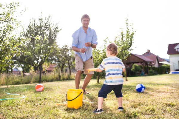 Menino com pai brincando com armas de água, salpicando — Fotografia de Stock