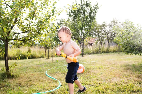 Menino com pistola de água salpicando alguém, garde verão ensolarado — Fotografia de Stock