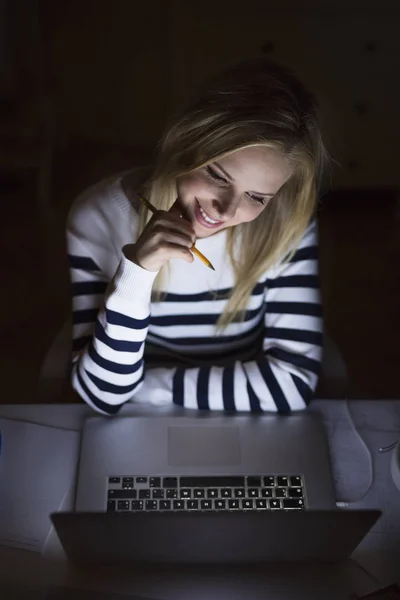 Kvinna sitter vid skrivbord och arbetar på laptop på natten. — Stockfoto