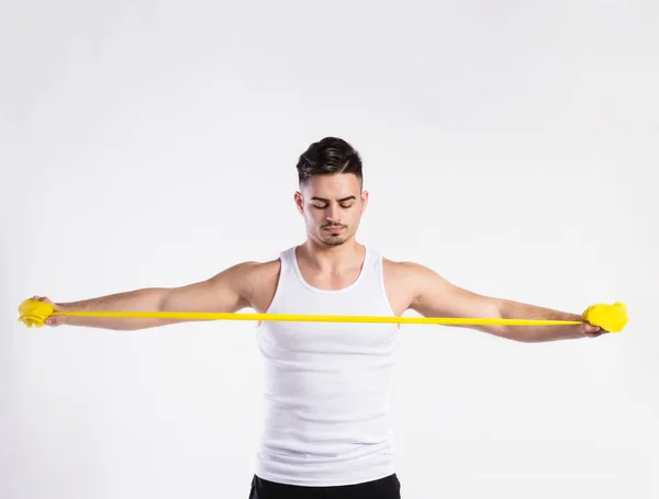Handsome fitness man working out with rubber band, studio shot. — Stock Photo, Image