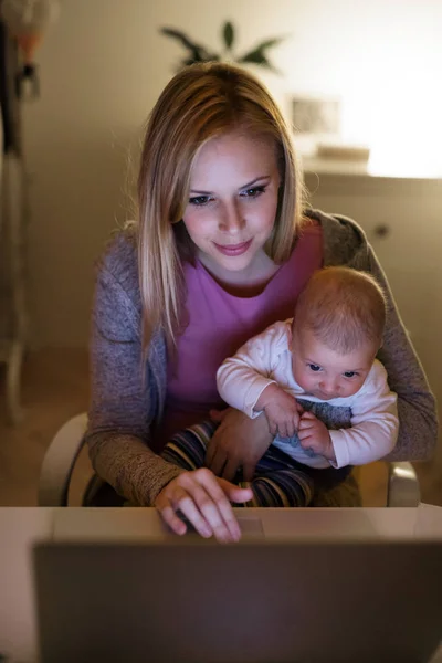 Madre con figlio tra le braccia, al lavoro sul computer portatile — Foto Stock