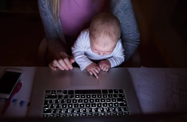 Неузнаваемая мать с сыном на коленях, работающая на ноутбуке — стоковое фото