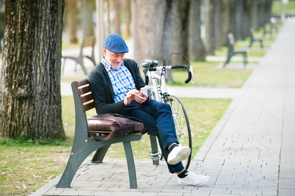 Uomo anziano con bicicletta in città, con in mano smartphone, sms — Foto Stock