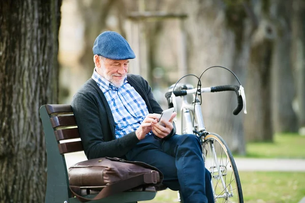 Homme âgé avec vélo en ville, tenant un téléphone intelligent, textos — Photo