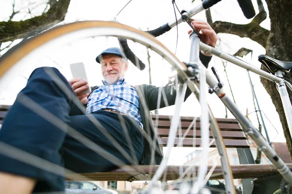 Homme âgé avec vélo en ville, tenant un téléphone intelligent, textos — Photo