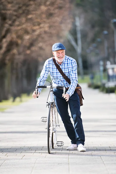 Senior man in blauwe ingecheckte shirt met fiets in de stad. — Stockfoto