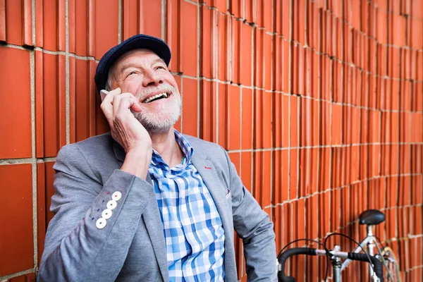 Starszy człowiek z smartphone i rower przed mur z cegły. — Zdjęcie stockowe