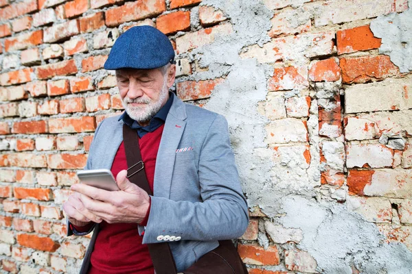 Äldre man med smartphone mot tegelvägg, textning. — Stockfoto