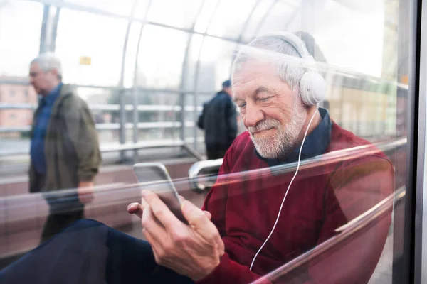 Homem sênior com smartphone e fones de ouvido sentado em passagem . — Fotografia de Stock