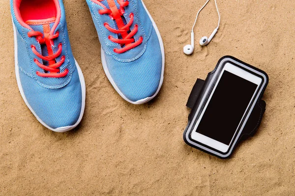 Sport skor, hörlurar, smartphone mot sand, studio skott. — Stockfoto