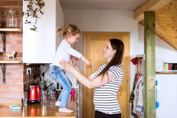 Mooie jonge moeder en dochtertje in de keuken. — Stockfoto